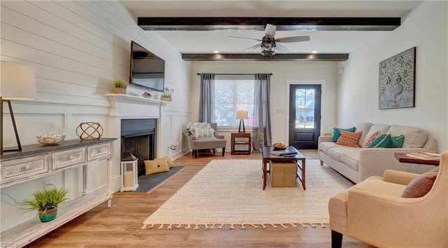 living room with a ceiling fan, light wood finished floors, beam ceiling, and a fireplace with flush hearth