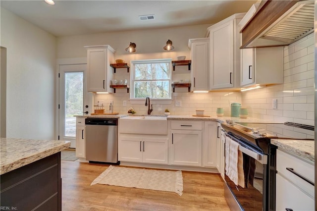 kitchen with visible vents, a sink, custom range hood, open shelves, and appliances with stainless steel finishes