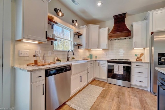 kitchen with a sink, stainless steel appliances, white cabinetry, visible vents, and premium range hood