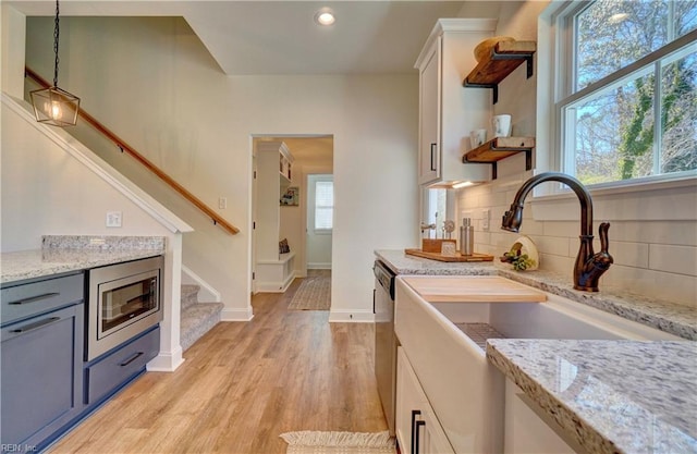 kitchen with a sink, stainless steel appliances, pendant lighting, light wood-type flooring, and decorative backsplash