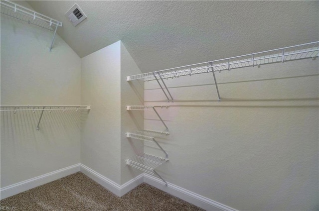 spacious closet with carpet flooring, visible vents, and vaulted ceiling