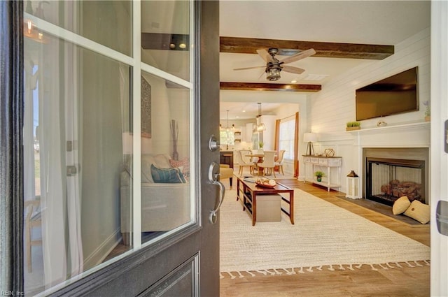 living area with ceiling fan, beam ceiling, a fireplace with flush hearth, and wood finished floors