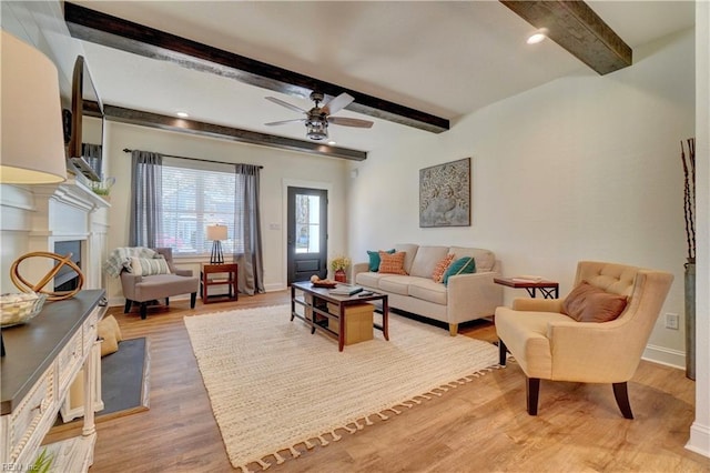 living room with a ceiling fan, a fireplace, baseboards, beamed ceiling, and light wood-style floors