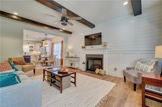 living area with light wood finished floors, beam ceiling, a fireplace with flush hearth, ceiling fan, and recessed lighting