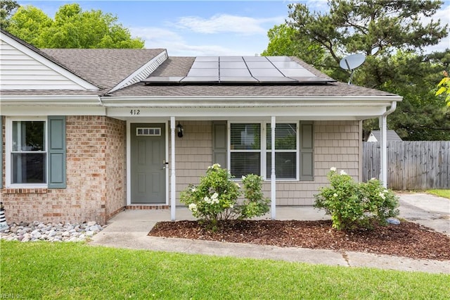 view of front of house featuring roof with shingles, solar panels, a porch, fence, and brick siding
