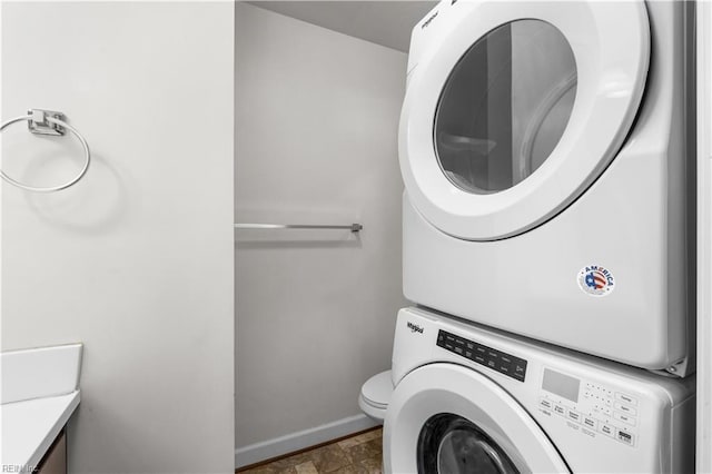 clothes washing area with stacked washer and clothes dryer, baseboards, and stone finish floors