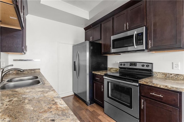 kitchen with appliances with stainless steel finishes, a sink, dark wood-type flooring, and dark brown cabinets