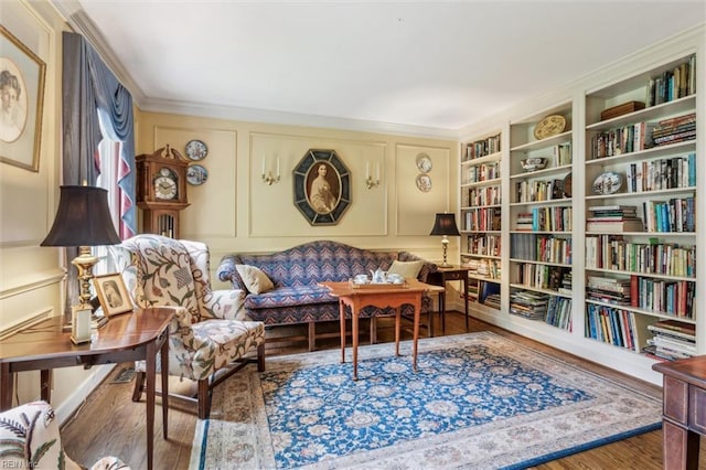 sitting room with a decorative wall, wood finished floors, bookshelves, ornamental molding, and built in shelves