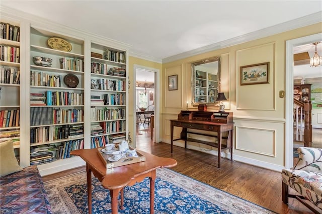 living area with a decorative wall, crown molding, bookshelves, and wood finished floors