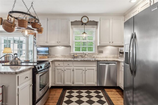 kitchen with stainless steel appliances, a sink, white cabinets, a peninsula, and wood finished floors