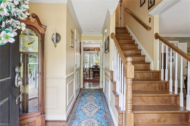 foyer with stairs, crown molding, a decorative wall, and a wainscoted wall