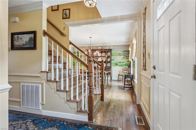foyer entrance featuring stairway, wood finished floors, crown molding, and a chandelier