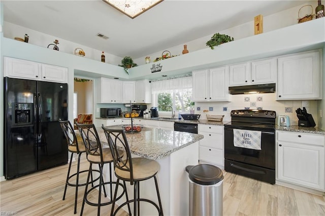 kitchen with black appliances, under cabinet range hood, a sink, white cabinetry, and light stone countertops