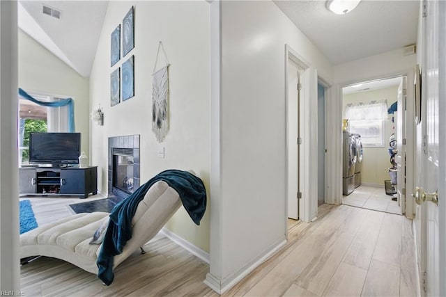 hall with washing machine and clothes dryer, light wood-type flooring, lofted ceiling, and plenty of natural light