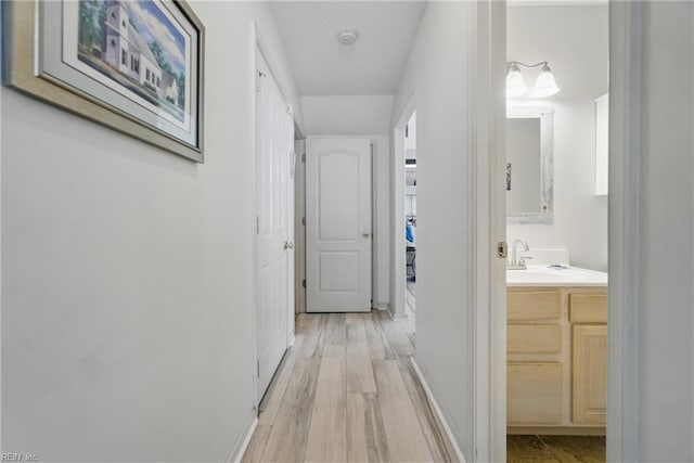 corridor with a sink, light wood finished floors, and baseboards