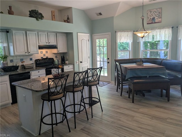 kitchen with black appliances, plenty of natural light, a kitchen breakfast bar, vaulted ceiling, and light wood-style flooring