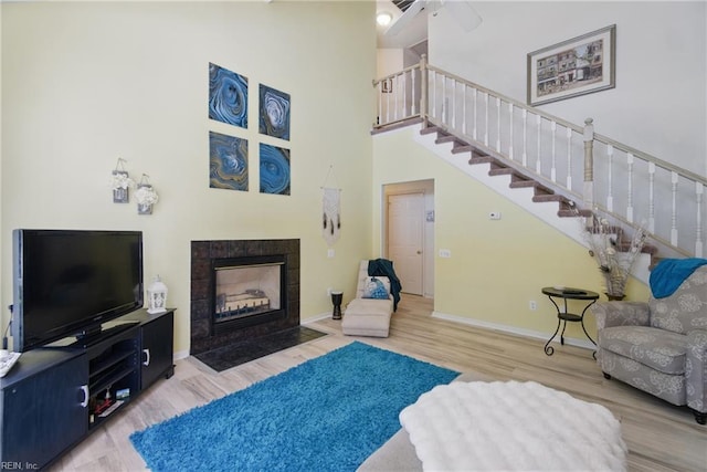 living area featuring stairway, wood finished floors, a fireplace, a high ceiling, and baseboards