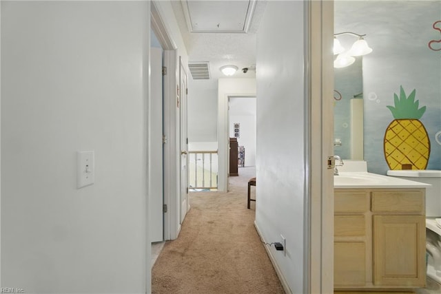 hallway featuring light colored carpet, a sink, and attic access