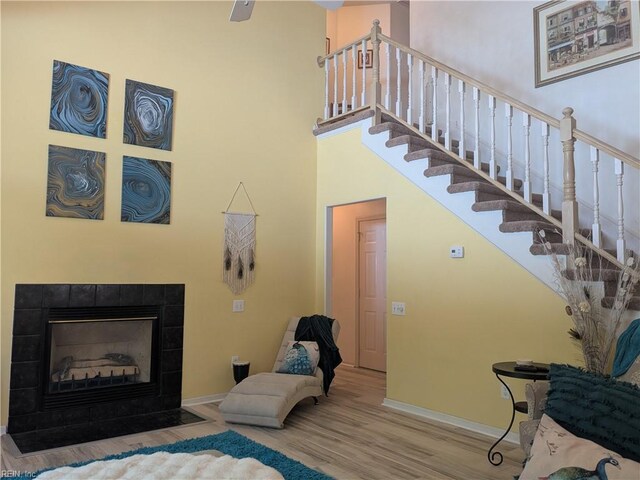 stairway with a towering ceiling, wood finished floors, baseboards, and a tile fireplace