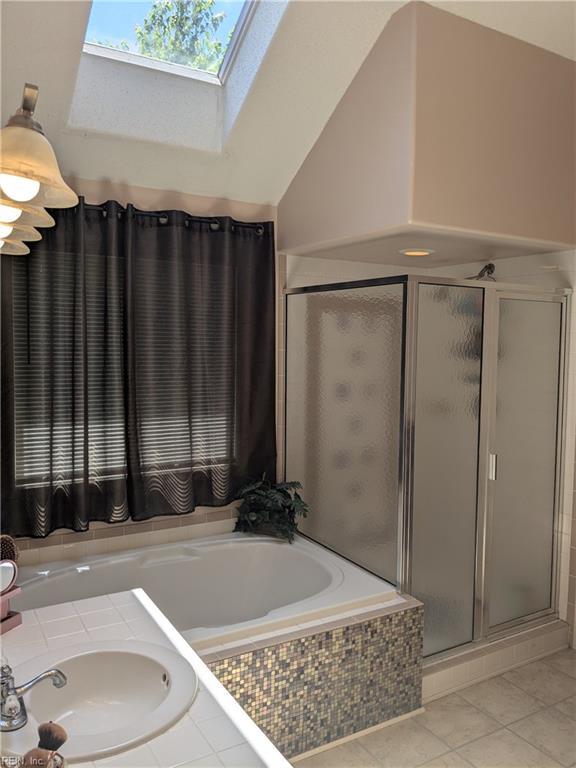 full bathroom with a sink, tile patterned floors, a stall shower, a skylight, and a garden tub