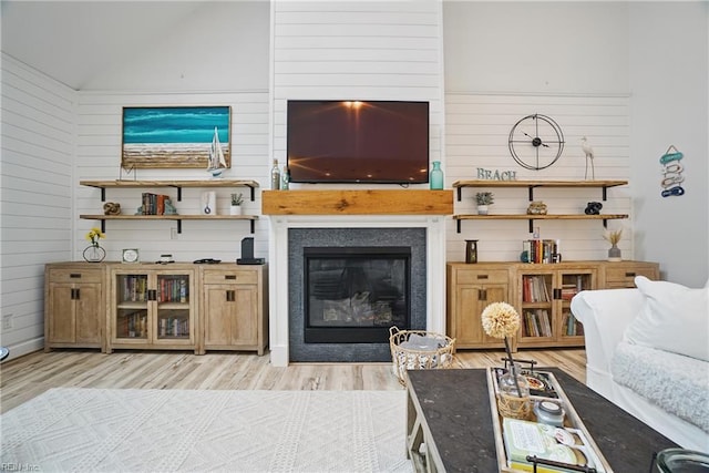 living area with light wood-type flooring, wooden walls, lofted ceiling, and a glass covered fireplace
