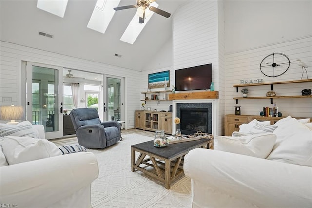 living room with high vaulted ceiling, ceiling fan, a skylight, a glass covered fireplace, and wooden walls