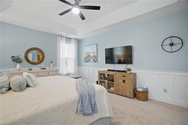bedroom featuring light carpet, a wainscoted wall, a ceiling fan, a decorative wall, and a tray ceiling