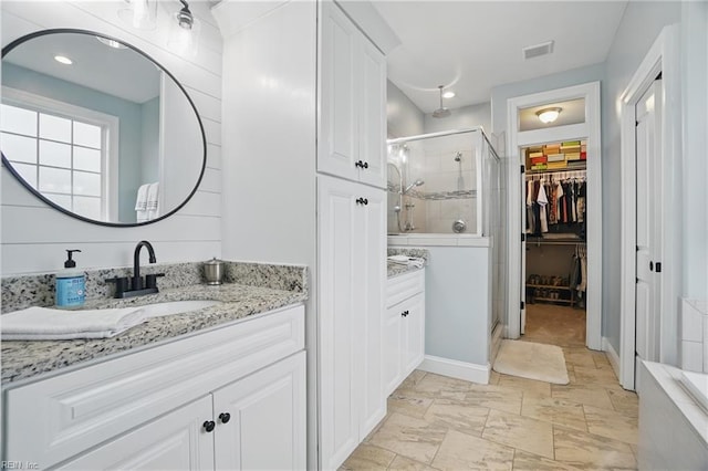 bathroom featuring a stall shower, vanity, a walk in closet, and baseboards