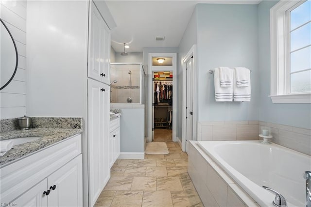 bathroom featuring vanity, a stall shower, a bath, a spacious closet, and baseboards