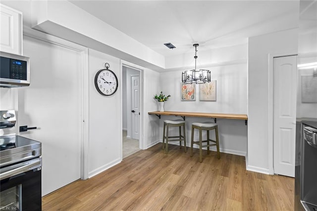 728 23rd St, Newport News, VA 23607 - kitchen featuring stainless steel appliances, a breakfast bar area, light wood finished floors, white cabinets, and a notable chandelier