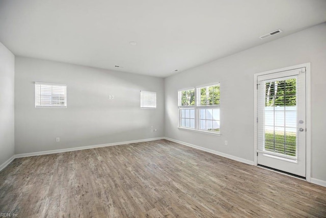 empty room with wood finished floors, visible vents, and baseboards