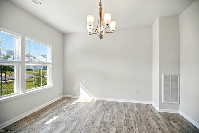 unfurnished room featuring visible vents, wood finished floors, baseboards, and a notable chandelier