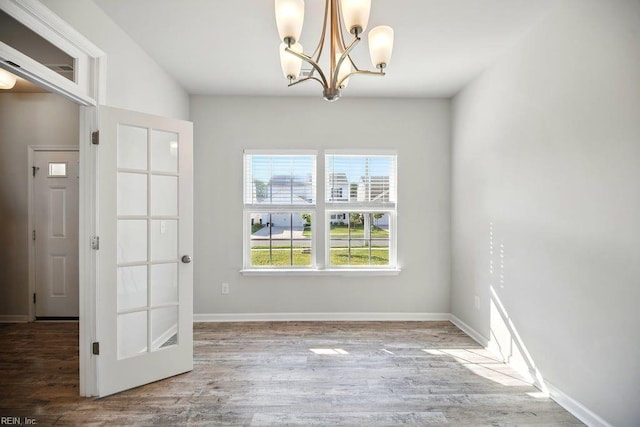 unfurnished dining area with a chandelier, baseboards, and wood finished floors