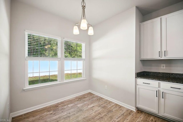 unfurnished dining area featuring baseboards, a notable chandelier, and light wood-type flooring