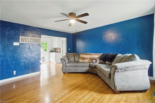 living room with light wood-style floors, baseboards, a ceiling fan, and an accent wall