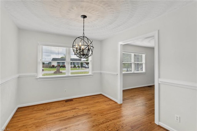 unfurnished dining area with wood finished floors, a chandelier, and baseboards