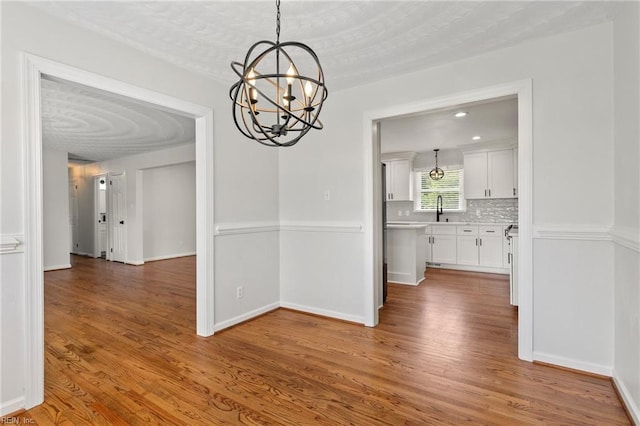 unfurnished dining area with a chandelier, wood finished floors, and baseboards