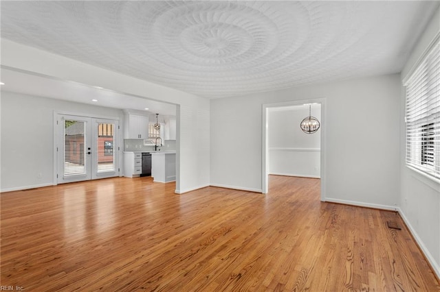 unfurnished living room with a chandelier, light wood finished floors, a sink, and baseboards