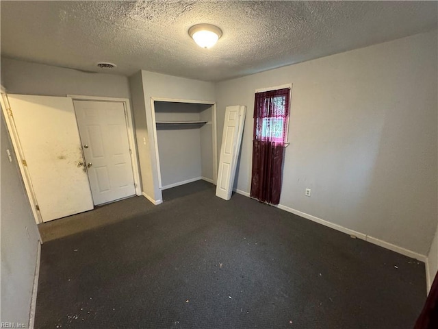 unfurnished bedroom with a closet, a textured ceiling, visible vents, baseboards, and dark carpet