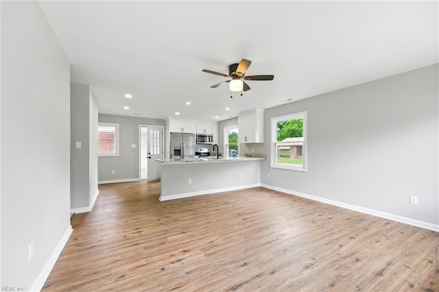 unfurnished living room with light wood-type flooring, plenty of natural light, baseboards, and a sink