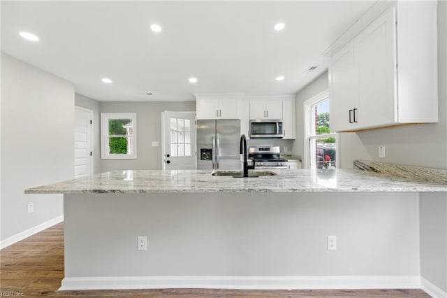 kitchen with a peninsula, light stone countertops, a wealth of natural light, and appliances with stainless steel finishes