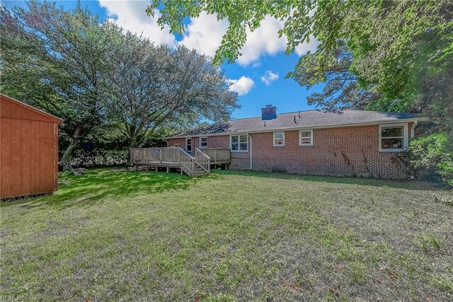 rear view of property with crawl space, a chimney, a lawn, a wooden deck, and brick siding