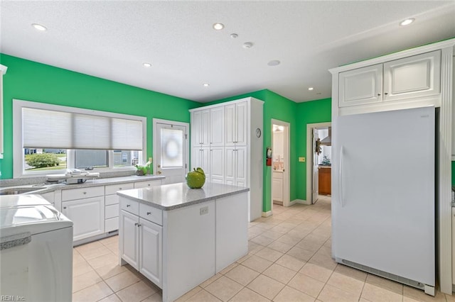 kitchen featuring freestanding refrigerator, a kitchen island, white cabinetry, washer / clothes dryer, and light countertops