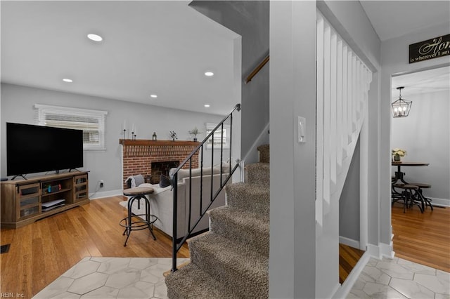 staircase with wood finished floors, a fireplace, recessed lighting, baseboards, and a chandelier