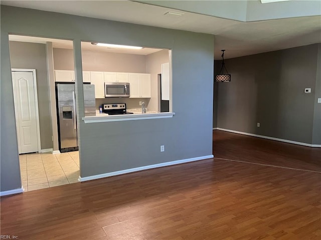 kitchen with wood finished floors, baseboards, white cabinets, and appliances with stainless steel finishes