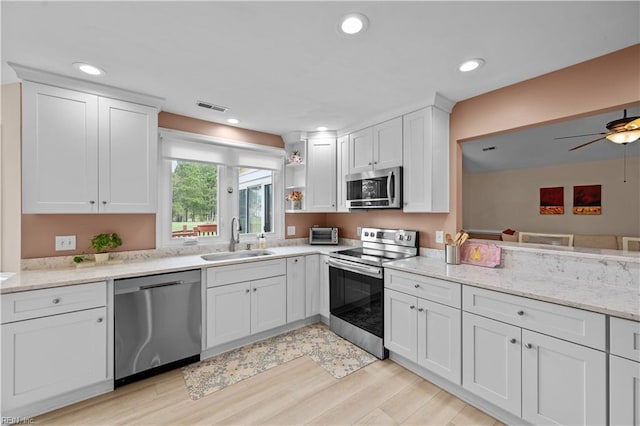 kitchen featuring appliances with stainless steel finishes, a sink, white cabinetry, light wood finished floors, and light stone countertops