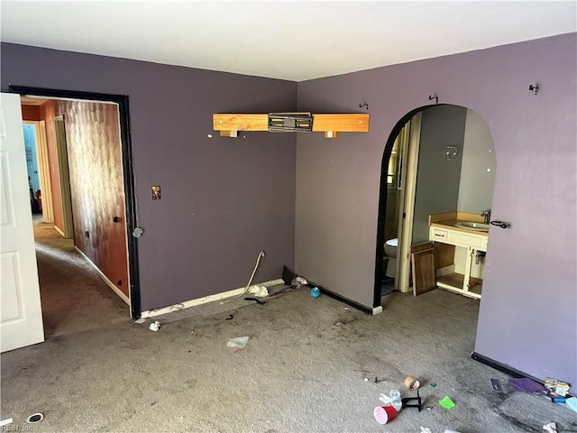spare room with carpet, arched walkways, a sink, and baseboards