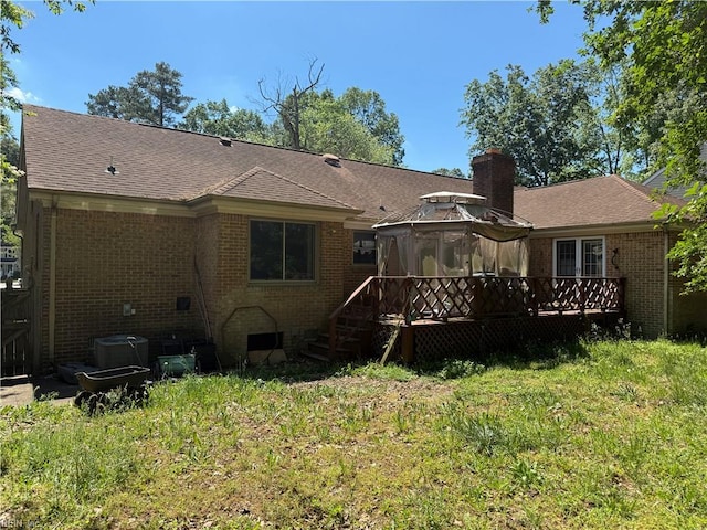 back of house with a gazebo, brick siding, a wooden deck, a lawn, and roof with shingles