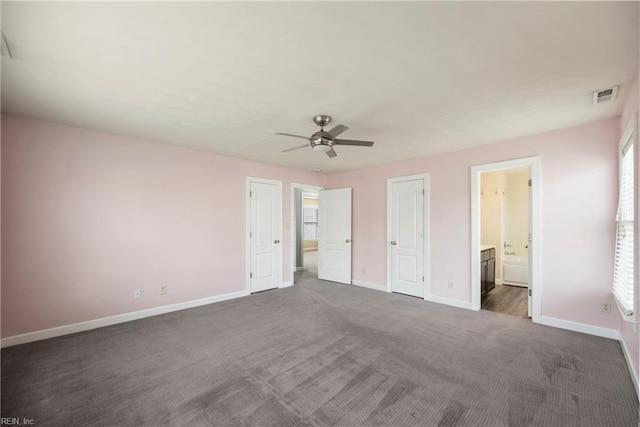 unfurnished bedroom with connected bathroom, visible vents, baseboards, ceiling fan, and dark colored carpet