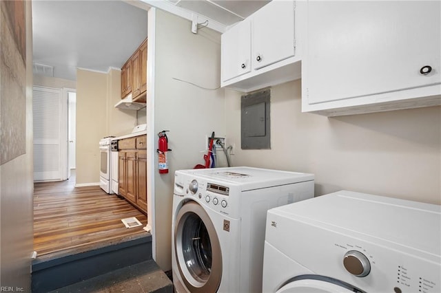 clothes washing area featuring washing machine and clothes dryer, electric panel, cabinet space, and wood finished floors